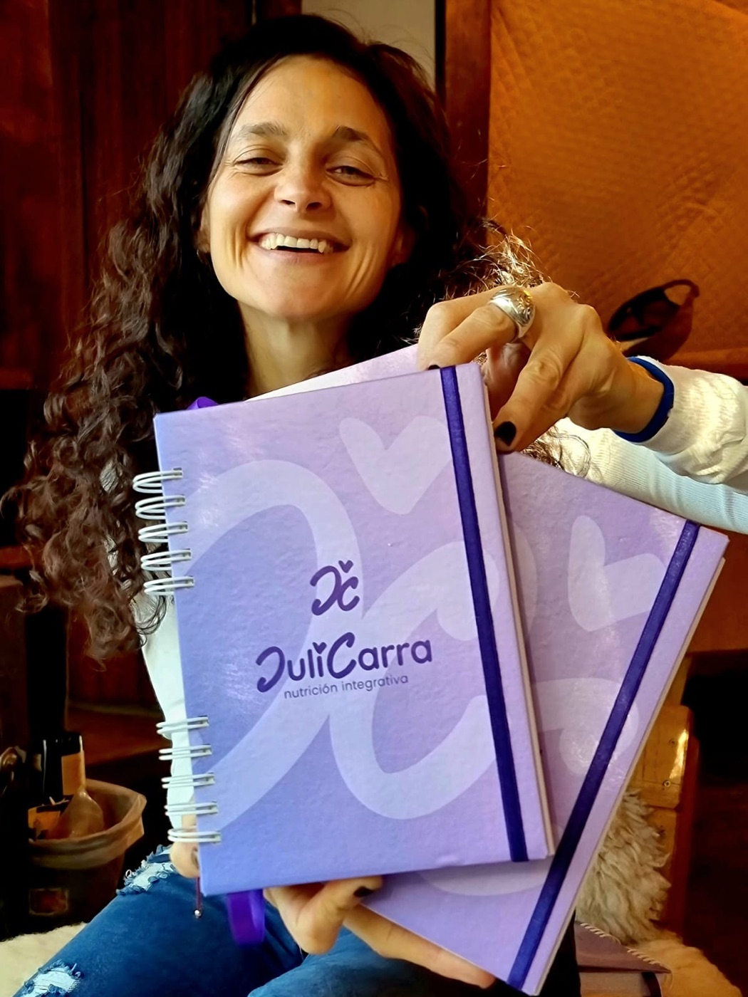 Juli sonriendo con los recetarios violetas de Juli Carra Nutrición Integrativa en la mano